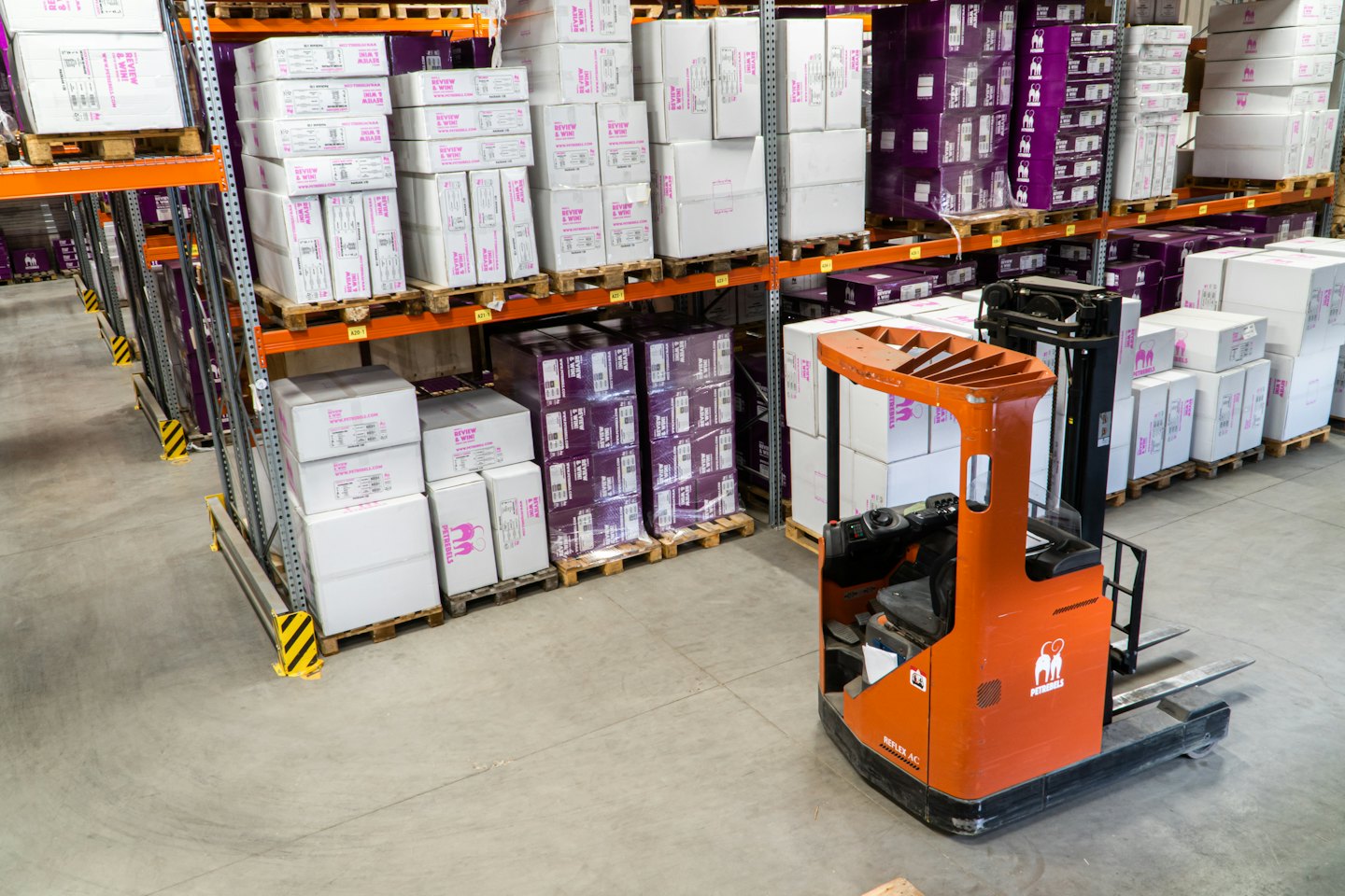 Yığılmış kutuların bulunduğu depoda park etmiş turuncu forklift.